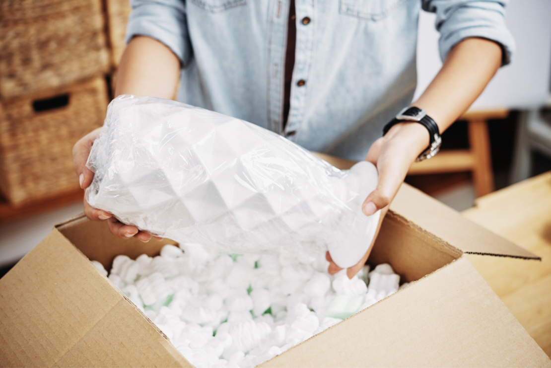 Woman puts a fragile vase in a box with packing peanuts.