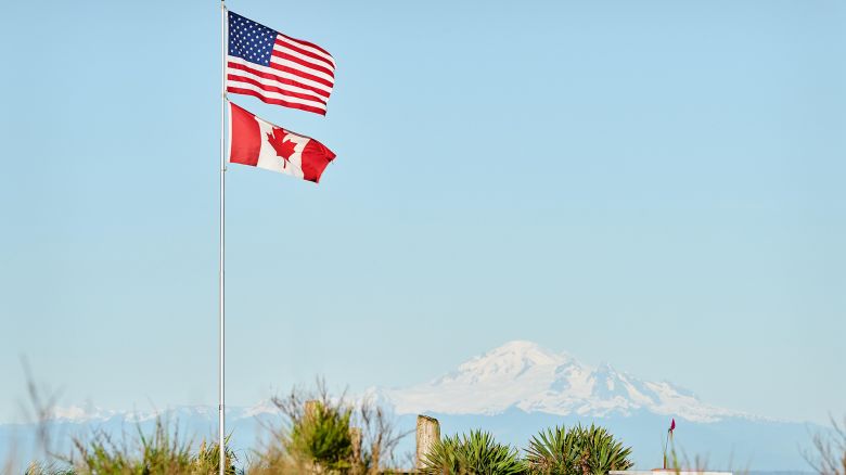 PEJ1YW US and Canadian Flag Together. US and Canadian Flags fly in Point Roberts, Washington State. The San Juan Islands in the background.