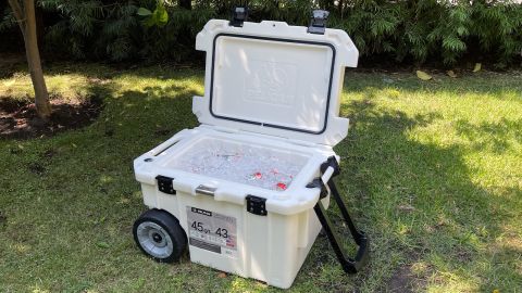 A white Pelican Elite 45 wheeled cooler, sitting in the shade on a green lawn.