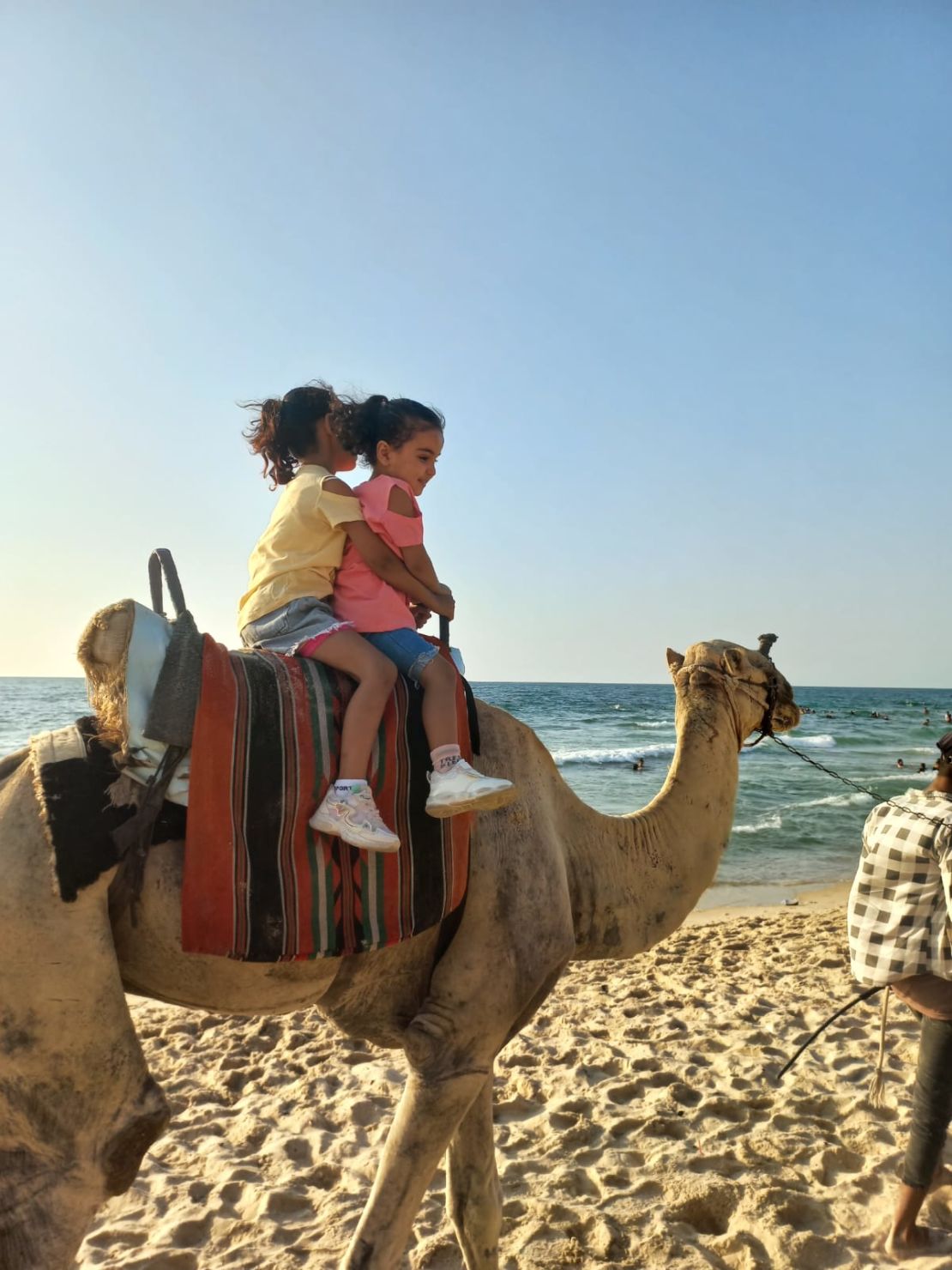 Palestinian siblings Ella Mohammed Hamouda (left) and Sila Mohammed Hamouda (right) ride a camel on a beach in northern Gaza, on October 6, 2023.