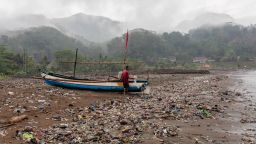 A local fisherman performs maintenance on his boat at Loji Beach, West Java, surrounded by garbage.