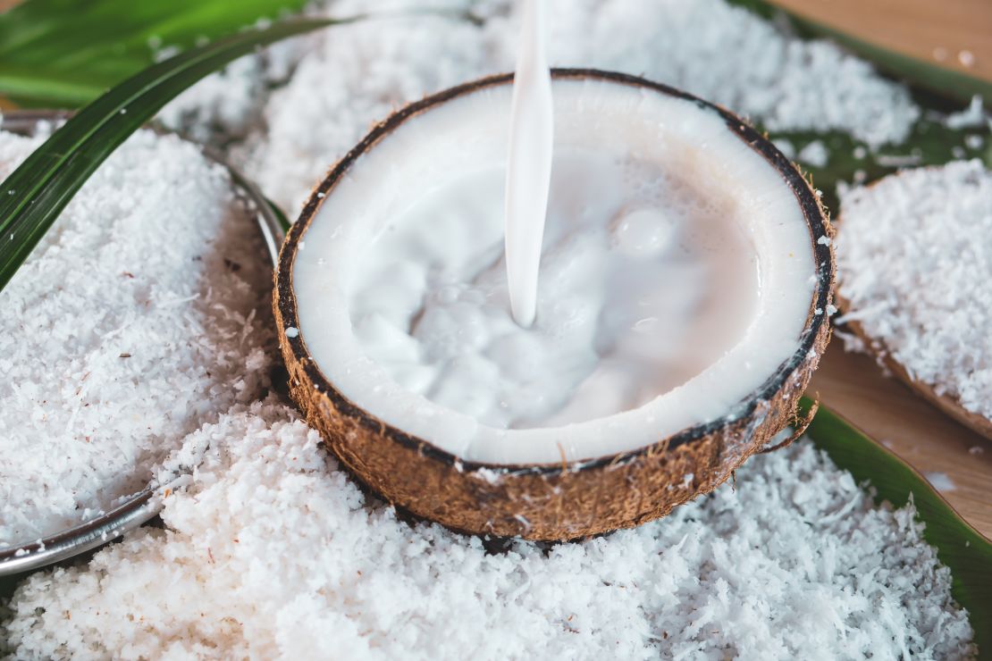 pouring-fresh-coconut-milk-into-halved-coconut-with-grated-coconut-background.jpg
