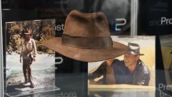 "Indiana Jones" brown fedora on display, in front of two photos of Harrison Ford in character wearing the hat, as part of the Propstore auction.