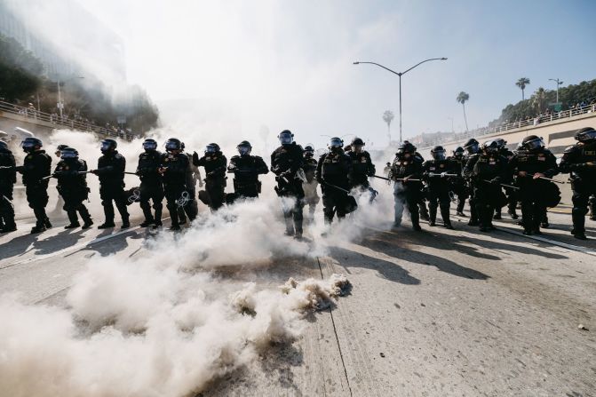 El humo llena el aire mientras agentes del orden con equipo antidisturbios avanzan durante las protestas en Los Ángeles el domingo.