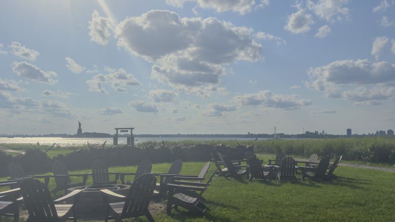 Landscape view of chairs with tables on grass and the Statue of Liberty in the distance.