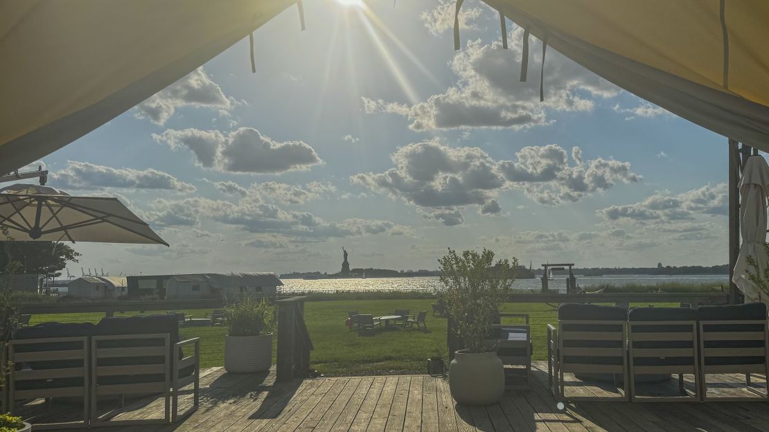 Landscape view of grass from inside of tent with the Statue of Liberty in the distance. 