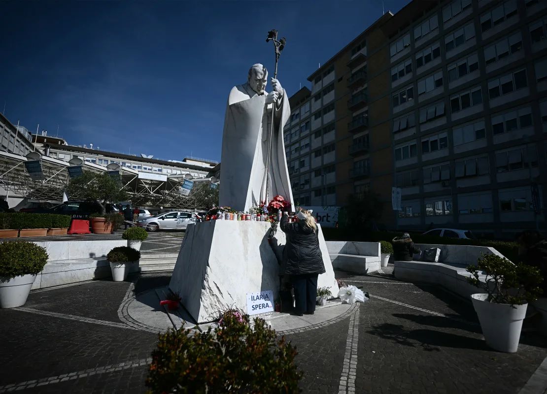 Una mujer deja un rosario a los pies de una estatua del difunto papa Juan Pablo II, el viernes, en el exterior del Policlínico Agostino Gemelli en Roma, Italia. El papa Francisco pasó allí su séptimo día, recibiendo tratamiento por neumonía.