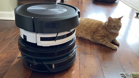 4 robot vacuums stacked, with a cat, on a hardwood floor