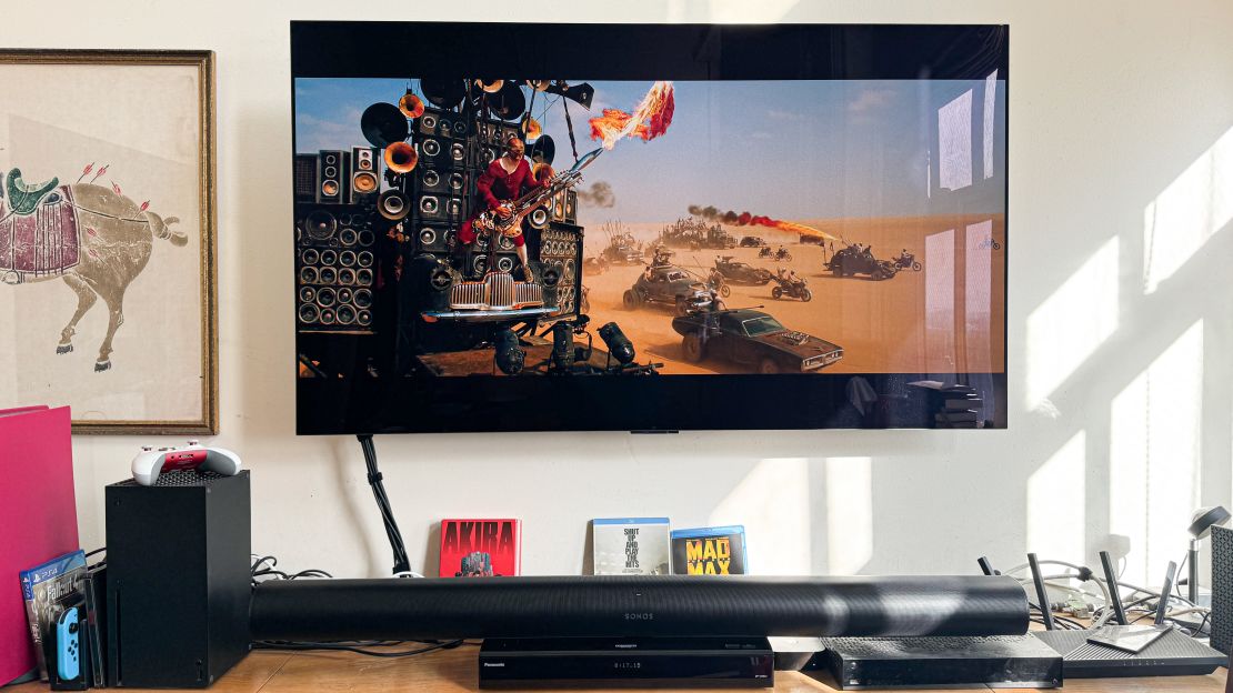 Above the Sonos Arc, the TV shows a masked guitarist with a flaming instrument riding on a vehicle full of speakers, as part of a massive convoy in "Mad Max: Fury Road."