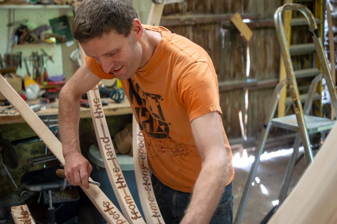 Artist Charlie Whinney places words onto the branches in his workshop.