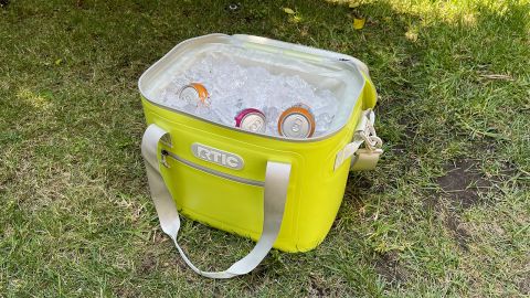 A lime-green RTIC Soft Pack 30 soft cooler, full of ice and drinks, on a grassy lawn