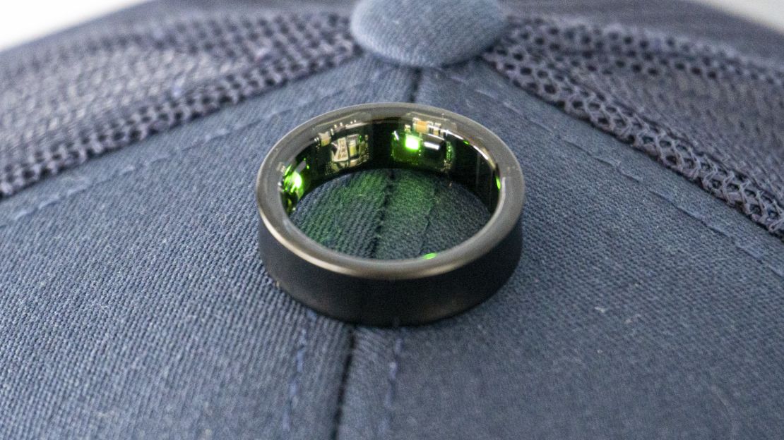 Black Samsung Galaxy Ring glowing with green lights and laying flat on top of a hat.