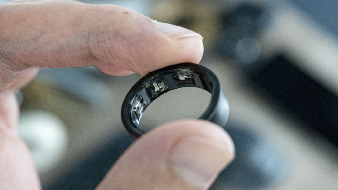 Fingers holding a black Samsung Galaxy Ring, showing the inside sensors.