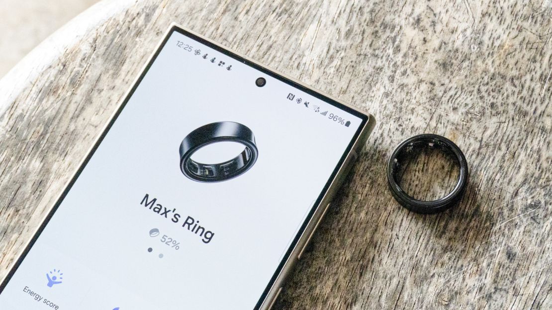 Black Samsung Galaxy Ring next to phone showing the ring's app.