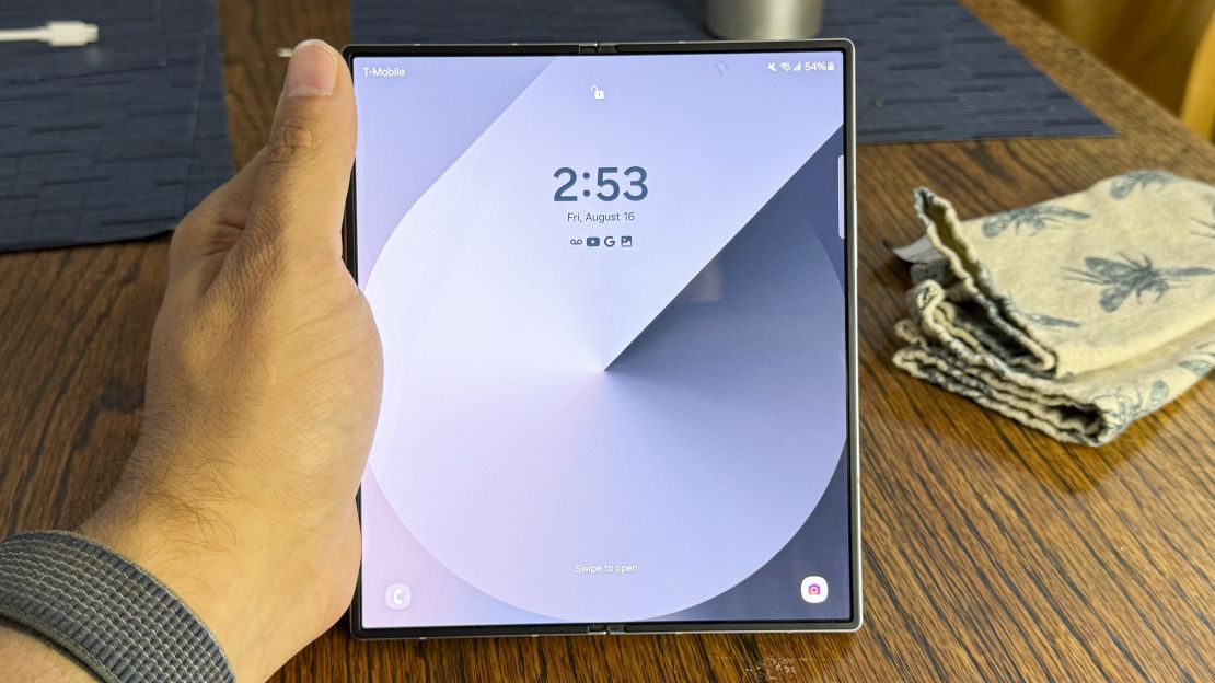 Samsung Galaxy Z Fold 6 is open in hand at a table, and its screen shows a gray lock screen