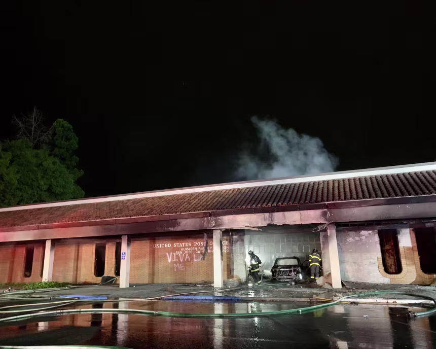 The front of the post office with firefighters inspecting the entrance after putting the fire out.