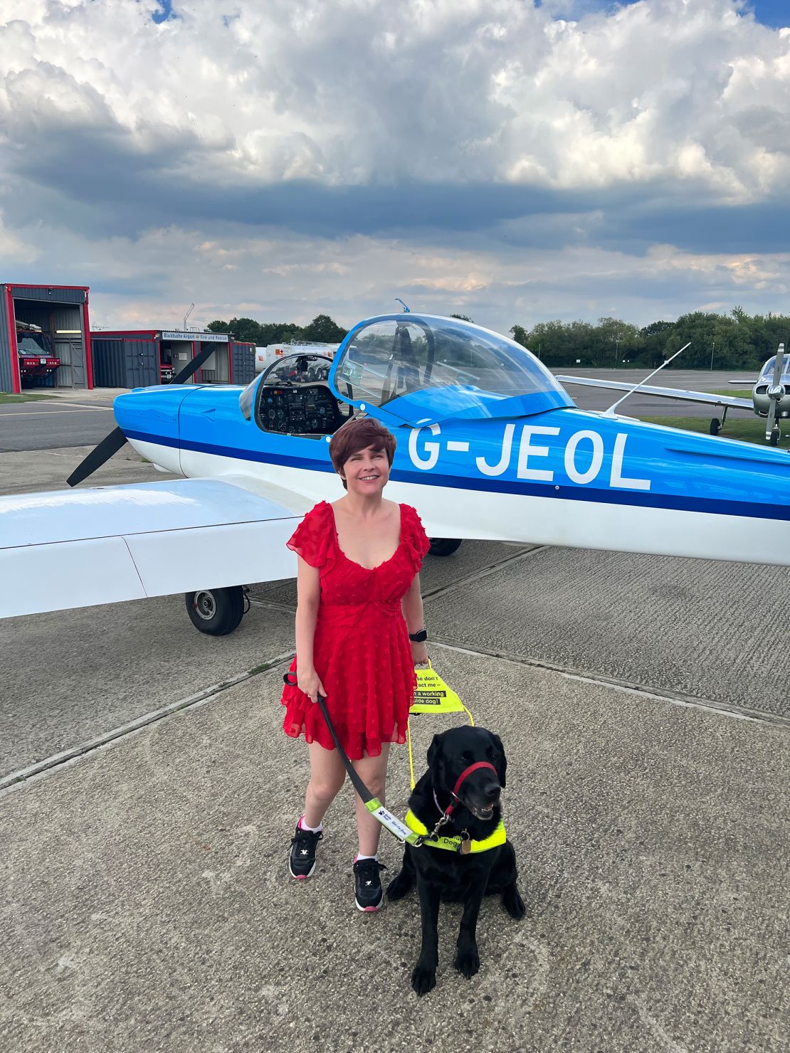 Sassy Wyatt and her guide dog, Ida, are pictured in front of a small airplane.