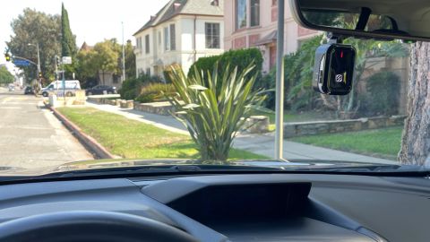A view from with a car equipped with a Scosche NEXS1 dash cam, mounted behind a car's mirror, a street scene is visible with the camera visible at upper right.