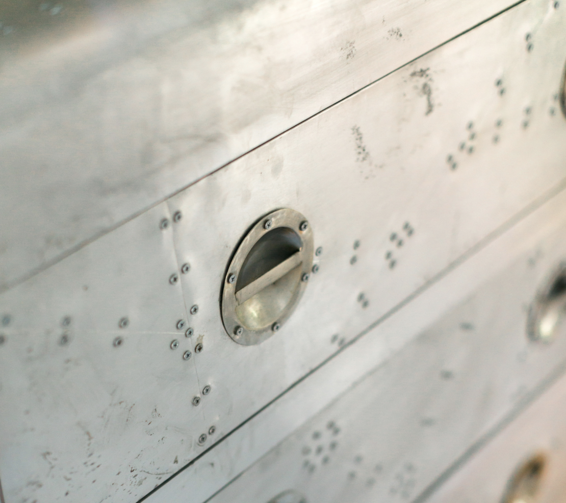 This vintage riveted metal chest has all the elements of metal, from the material itself to the silver-gray color to the round-shaped pulls.
