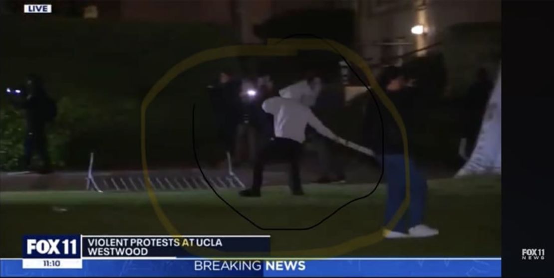 An image from Fox 11 Los Angeles posted on Facebook by Sharon On-Siboni shows her son, Edan On, with a white hoodie throwing an object into the encampment created by pro-Palestinian protesters at UCLA. On-Siboni highlighted the image.