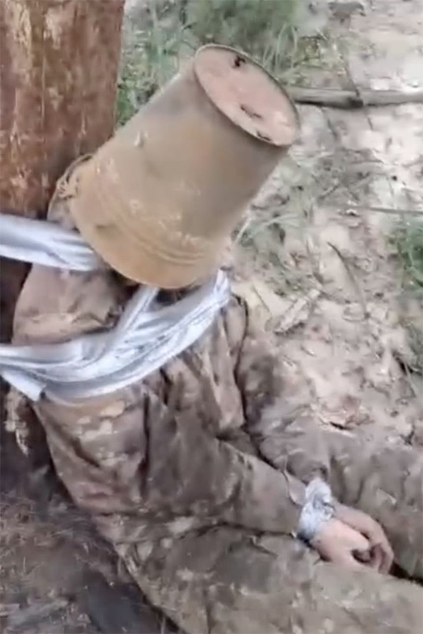 In another video, a man is tied to a tree with a rusty bucket over his head. After the bucket is removed, he is kicked repeatedly in the face.