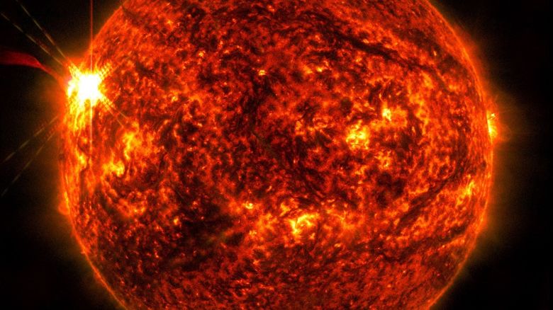 El Observatorio de Dinámica Solar de la NASA capturó esta imagen de una llamarada solar (vista como el destello brillante a la izquierda) el 14 de mayo. La imagen muestra un subconjunto de luz ultravioleta extrema que resalta el material extremadamente caliente en las llamaradas y que está coloreado en rojo.
