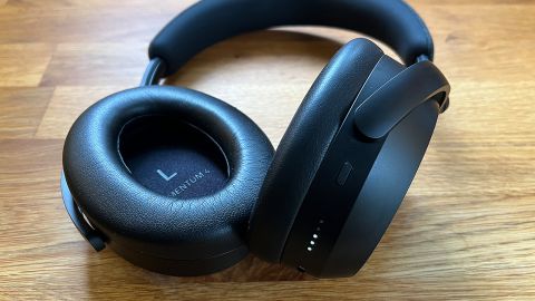 A pair of Sennheiser Momentum 4 headphones on a wooden countertop, showing details on the inside and outside of the earcups.
