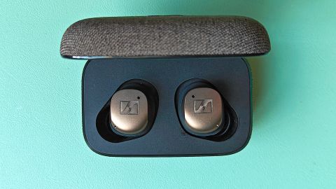 Sennheiser Momentum True Wireless 4 earbuds in their case while resting on a teal surface.