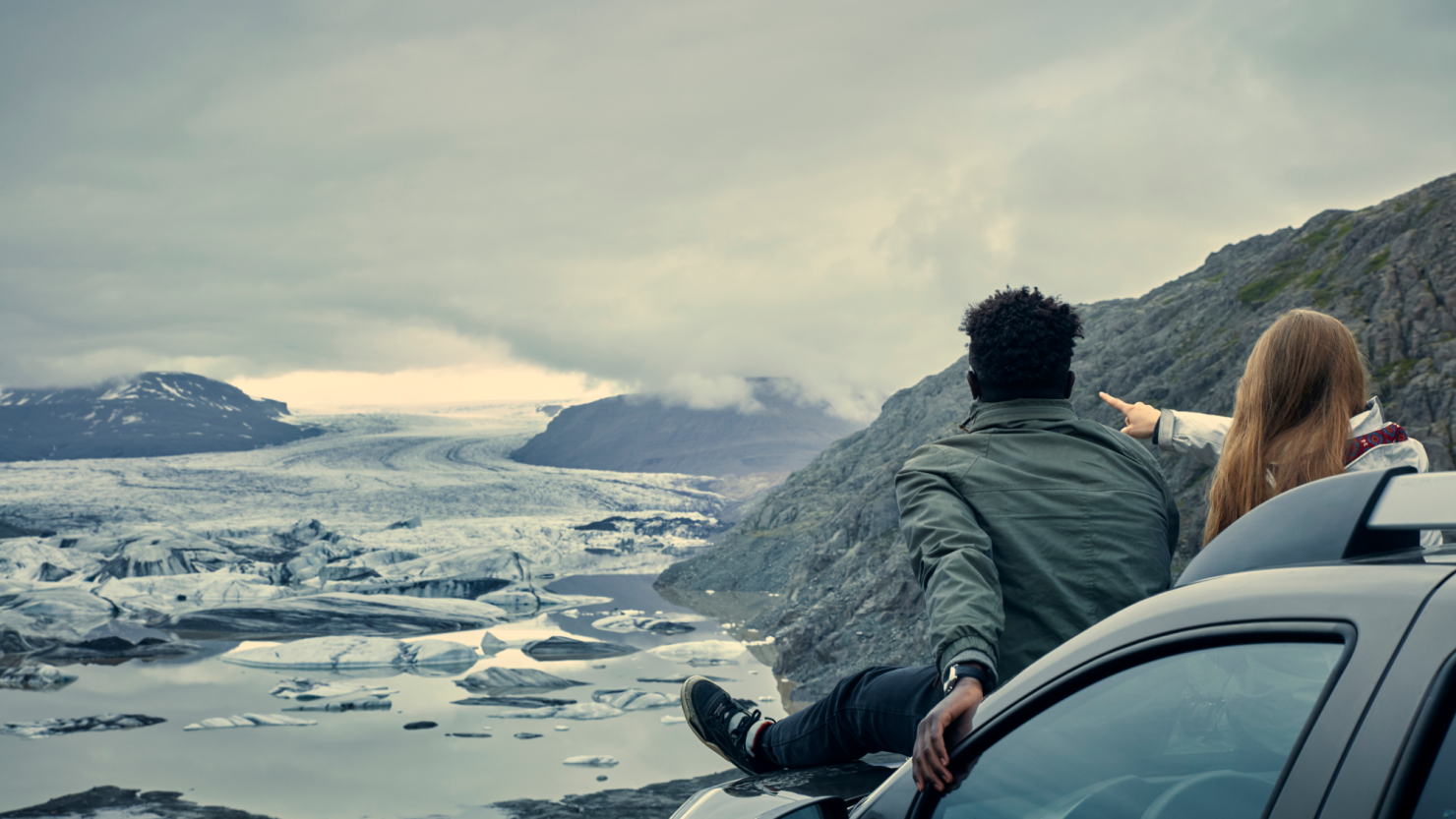 Couple sits on a car hood overlooking an Alaskan landscape.