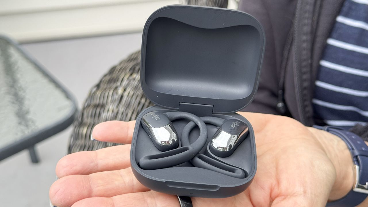 Person holding the Shokz OpenFit Air headphones and case.