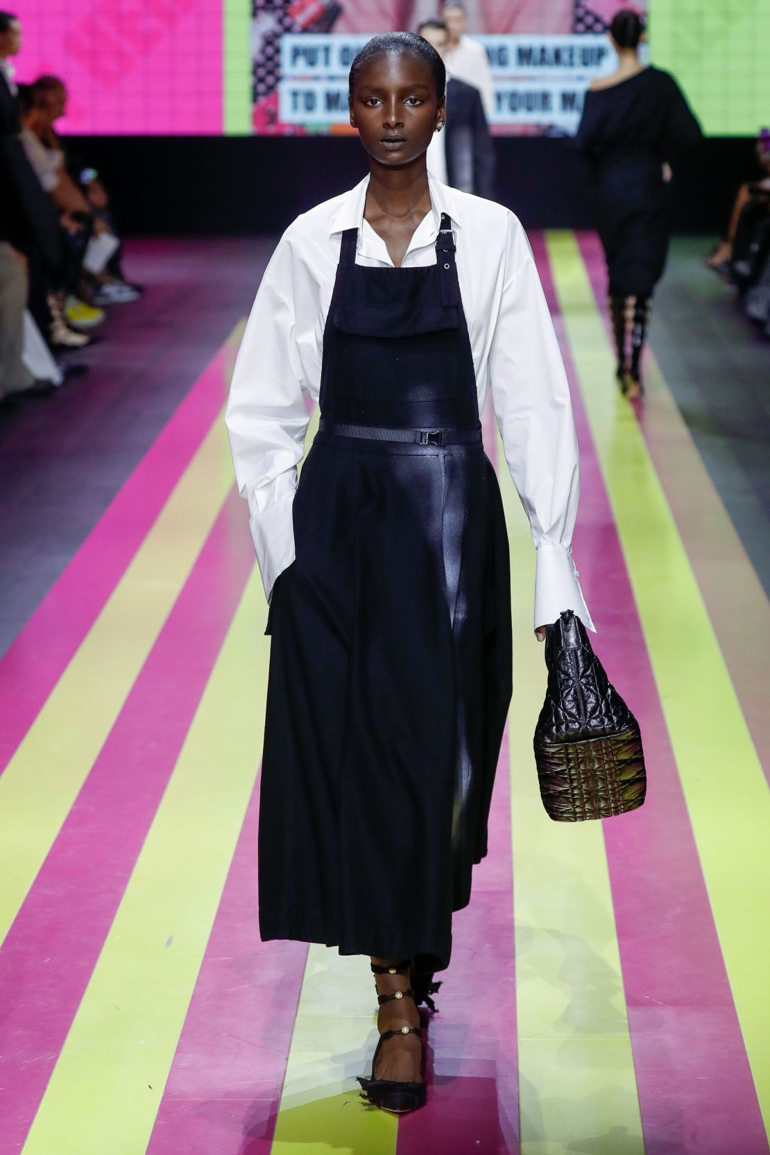 Een model loopt door de catwalk voor Dior, in een zwart schort van de volledige lengte, september 2023.