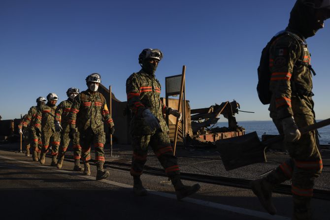 A Mexican search-and-rescue team walks alongside a road overlooking burned homes in Malibu.