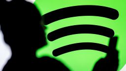In this photo illustration, a woman seen looking at a smartphone with a Spotify logo displayed in the background.