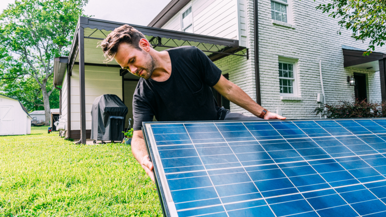 Man inspects a solar panel in front of a house.