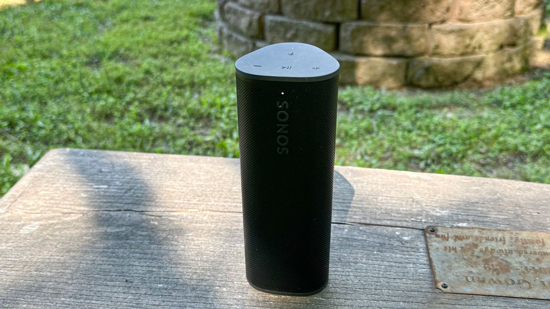 A Sonos Roam 2 speaker on a stone surface in a grassy backyard.