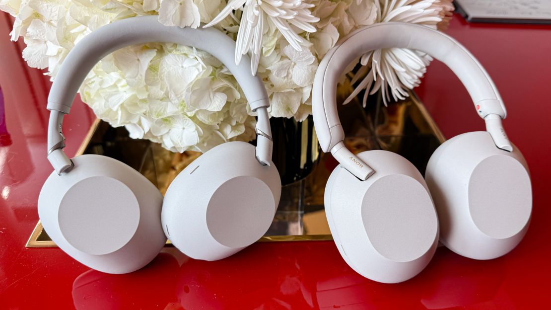 The white Sony XM6 and XM5 headphones on a table in front of a white flower