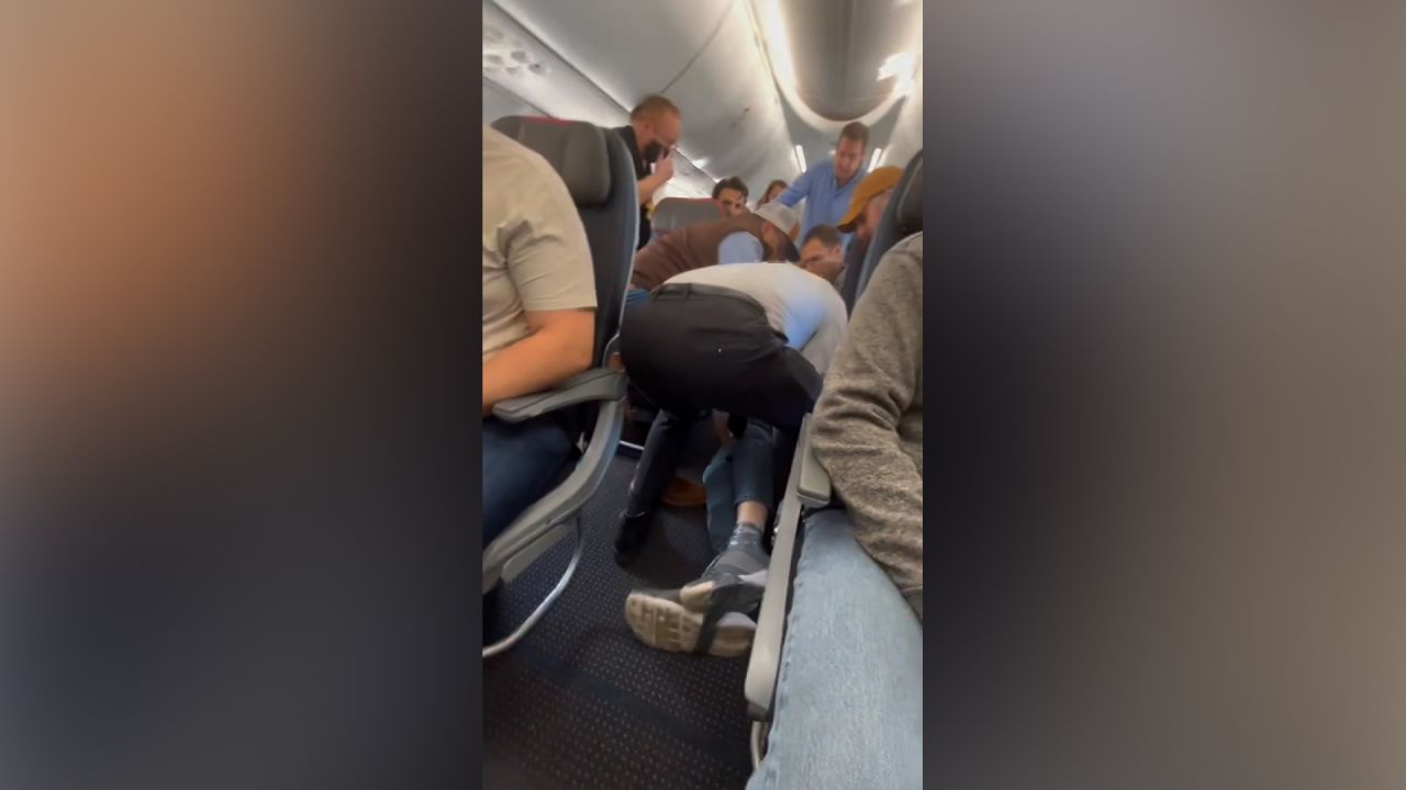 An Albuquerque, New Mexico flight was forced to return "shortly after takeoff due to a disturbance" with a disruptive passenger Tuesday afternoon, according to an American Airlines spokesperson. Video taken by passenger Zach Etkind on the plane shows a scuffle on the aisle floor while several men are subduing a person. Etkind told CNN multiple male passengers pulled him to the ground and flight attendants restrained him with duct-tape and flexi cuffs.