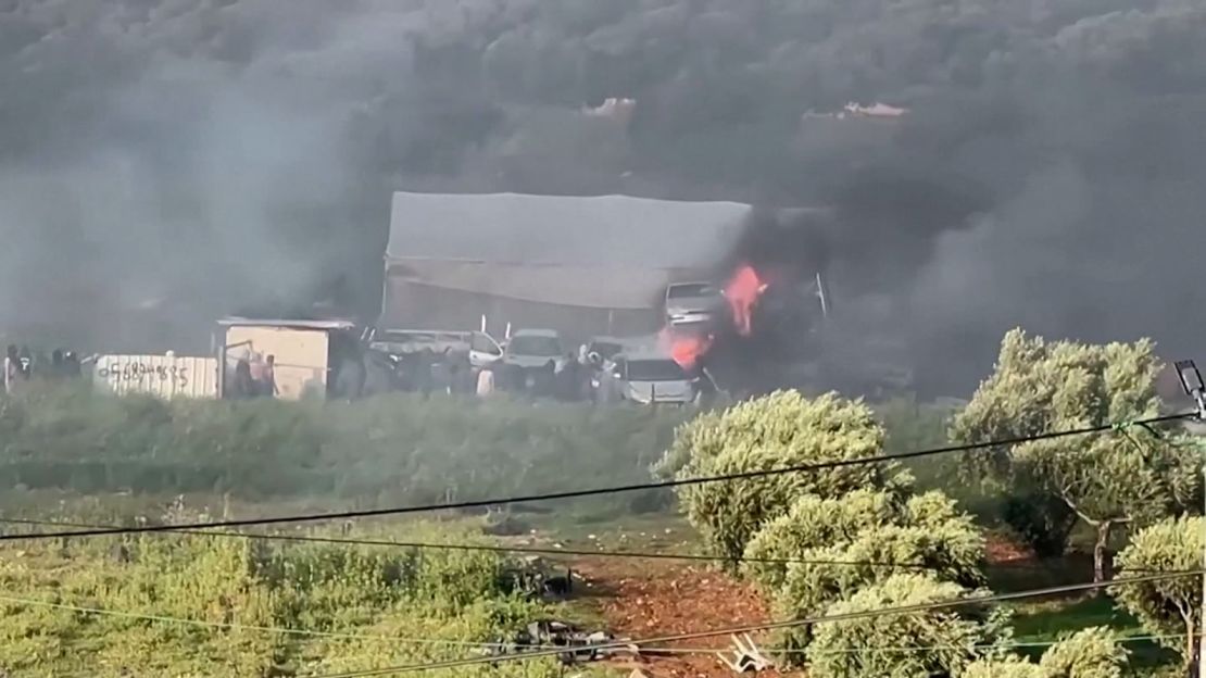 Israeli settlers wearing headscarves are seen near billowing smoke.