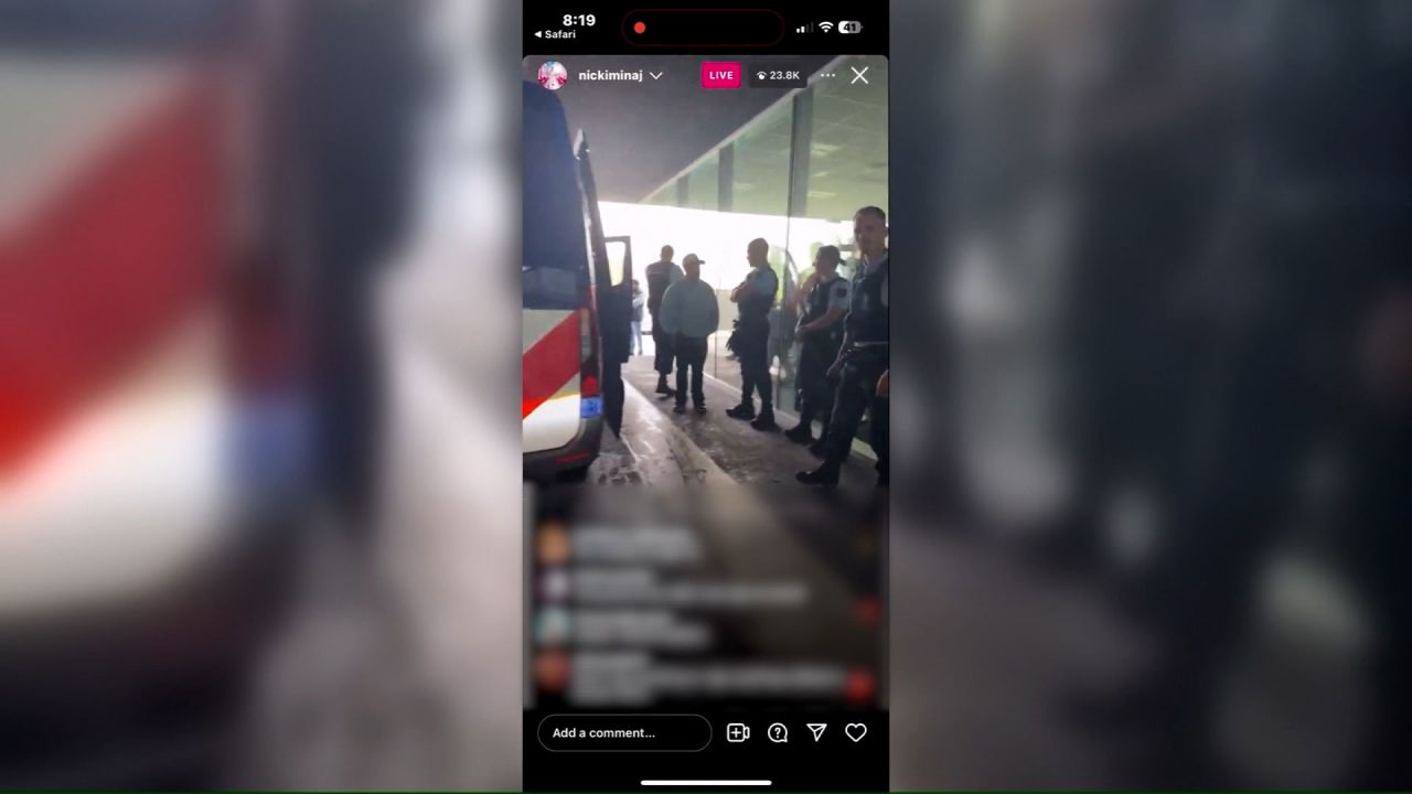 In this still from Nicki Minaj's Instagram Live, the rapper is ushered out of her vehicle by police at Amsterdam’s Schiphol Airport. CNN has blurred the comments on the livestream.