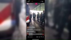 In this still from Nicki Minaj's Instagram Live, the rapper is ushered out of her vehicle by police at Amsterdam’s Schiphol Airport. CNN has blurred the comments on the livestream.