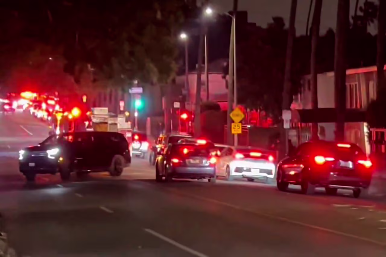 This screenshot from a video taken at Sunset Boulevard shows rows of vehicles leaving the area as first responders rush to the scene.