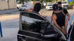 This video shows an ICE arrest taking places as two masked agents put a cuffed man into a car.