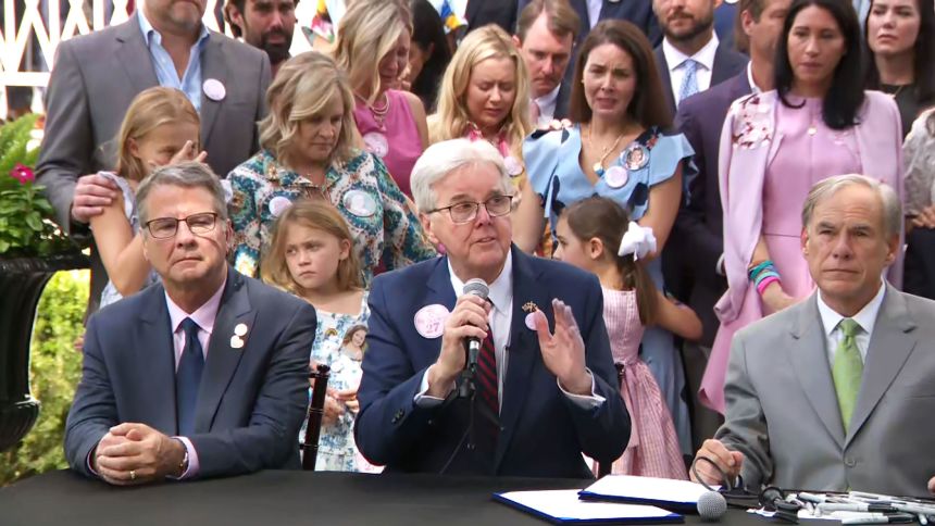 Families of the Camp Mystic campers and counselors flank Lt. Gov. Dan Patrick and Gov. Greg Abbott at a signing ceremony for camp safety on Friday in Austin.