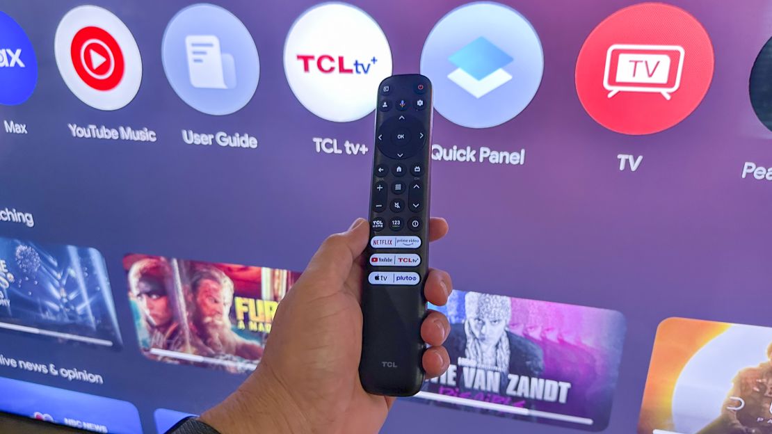 TCL QM8 TV in the background showing apps available on screen, with the remote control in the center in front of the TV.