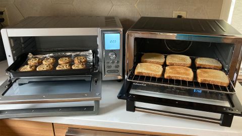 Two open toaster ovens, one displaying a tray of freshly-baked cookies, the other 6 slices of toast