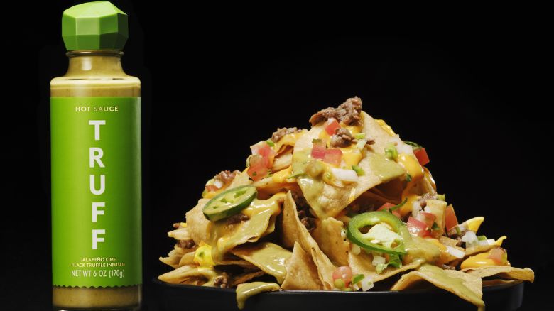 A bottle of green hot sauce and a pile of nachos.