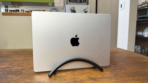 A MacBook stands upright on the black Twelve South BookArc Flex on a wooden table