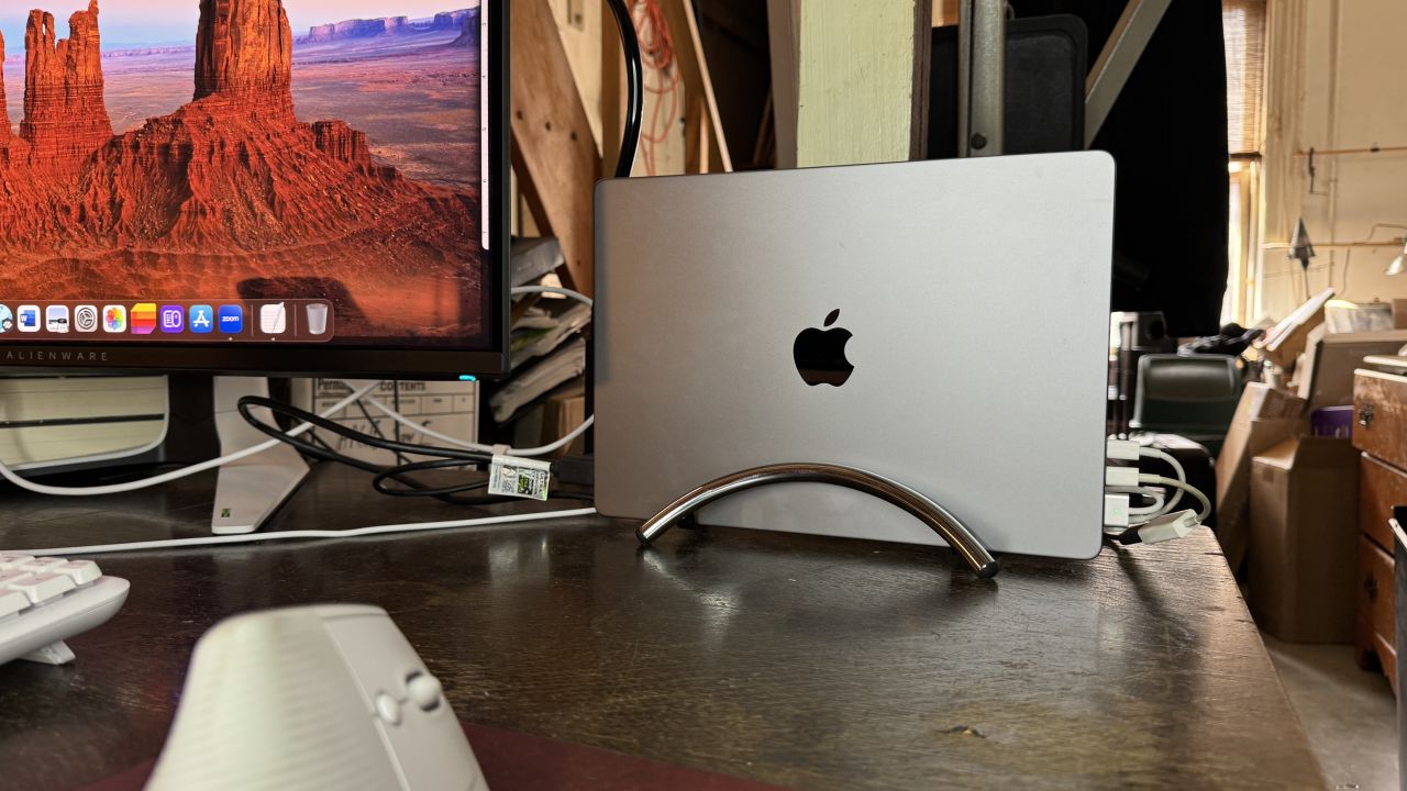 A MacBook stands upright in the chrome Twelve South BookArc Flex at a desk.