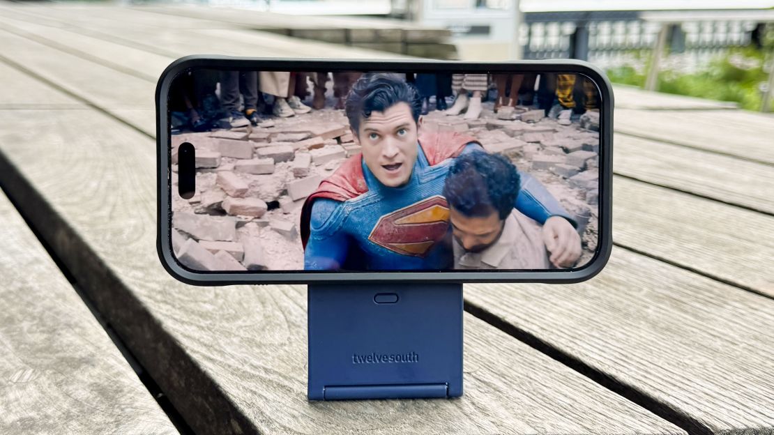 An iPhone showing the Superman trailer is in horizontal orientation, raised aloft by the Twelve South Curve Nano, sitting on wood