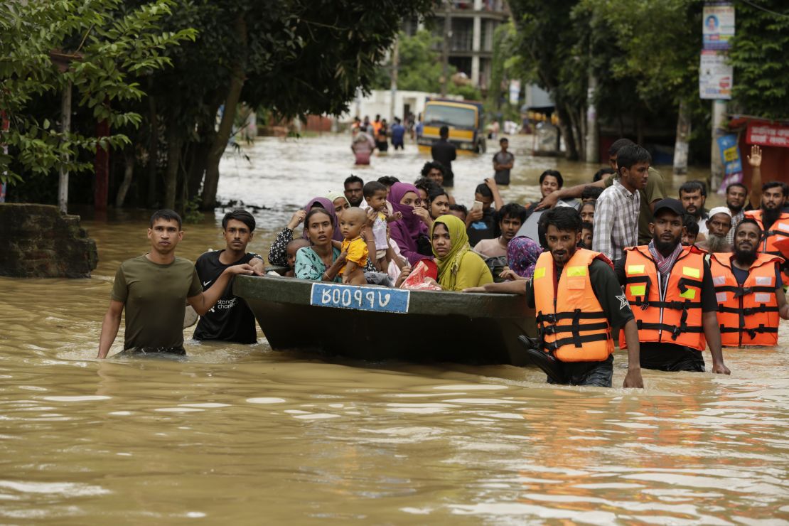 Rescuers in orange life vests escort stranded people to higher ground in Bangladesh.